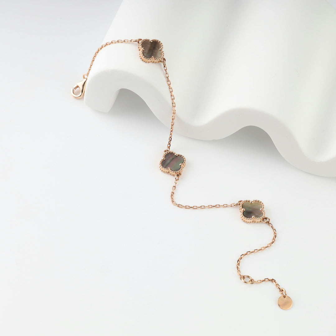 Rose gold clover bracelet with grey mother-of-pearl draped over a white display stand